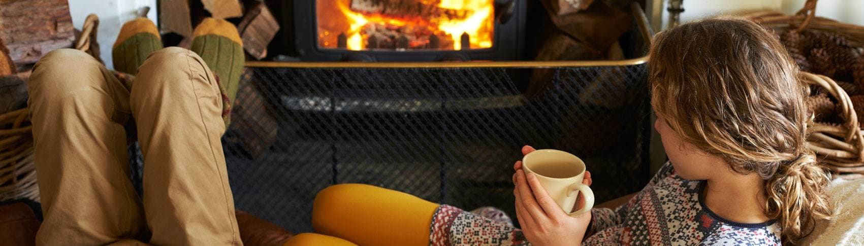 Bild: Kvinna som ligger framför brasa med kaffekopp