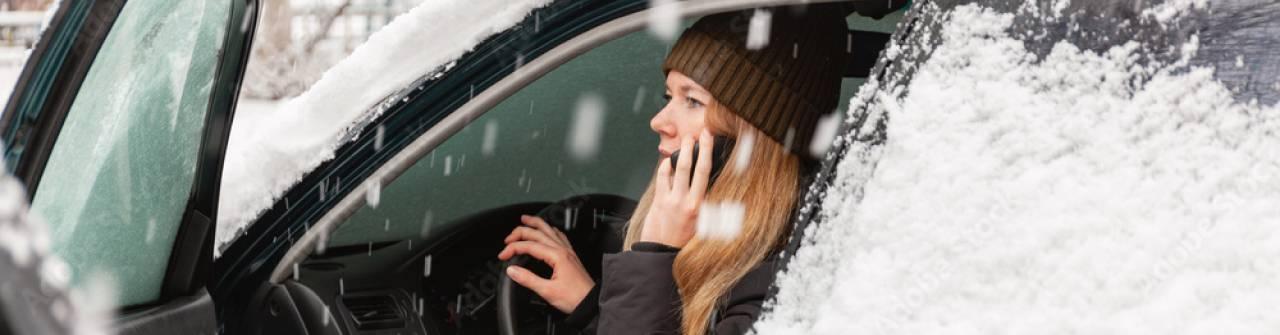 Kvinna sitter i sin bil och pratar i mobiltelefonen. Bildörren är öppen.