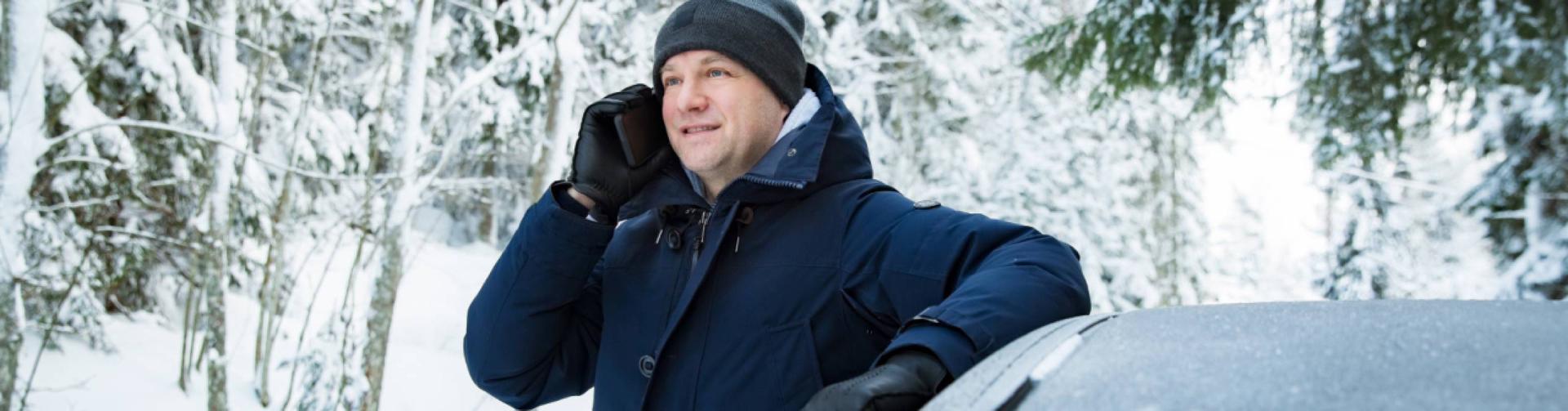 man som lutar sig mot bil och pratar i telefon i en snöig skog
