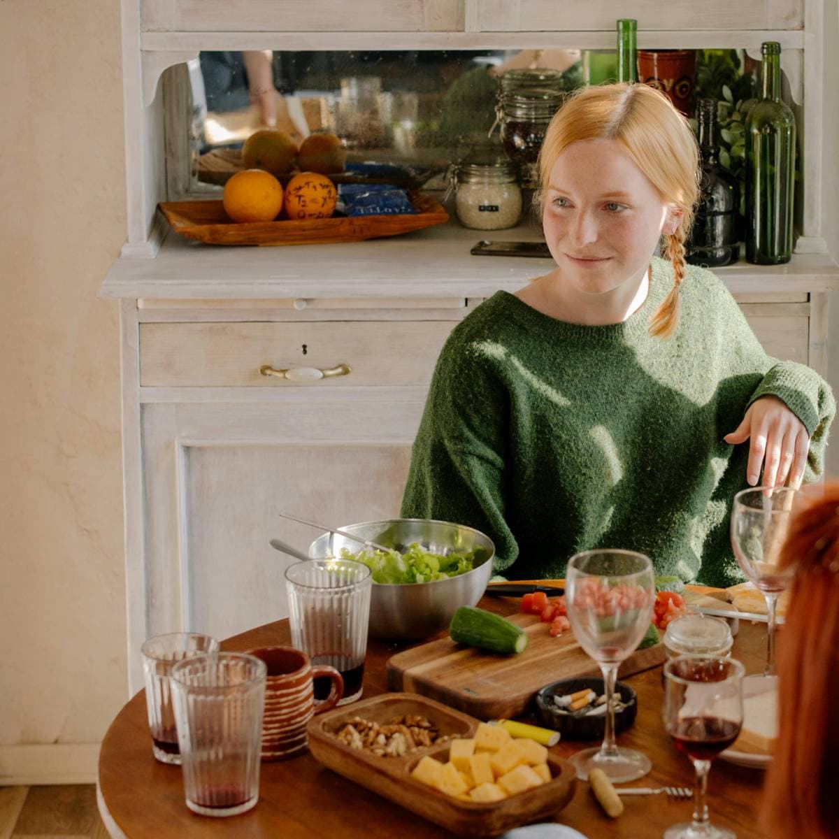 Kvinna med flätor och grön tröja sitter vid ett matbord