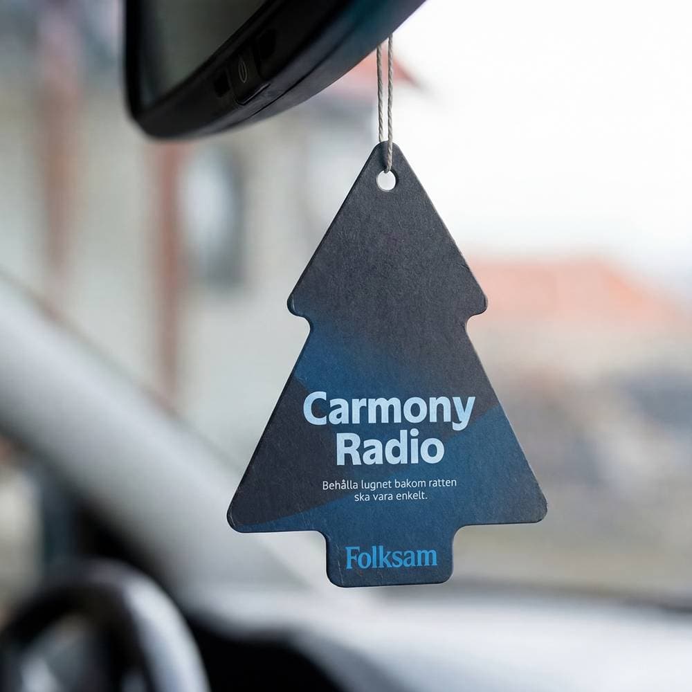 En doftgran med texten Carmony Radio hänger på backspegeln i en bil 