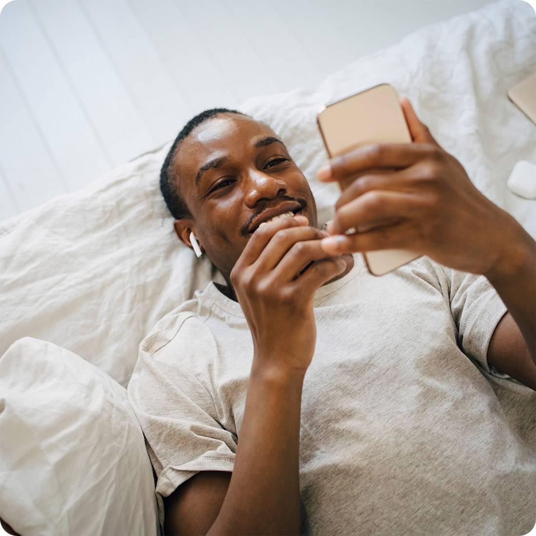 Person i säng med mobiltelefon i handen