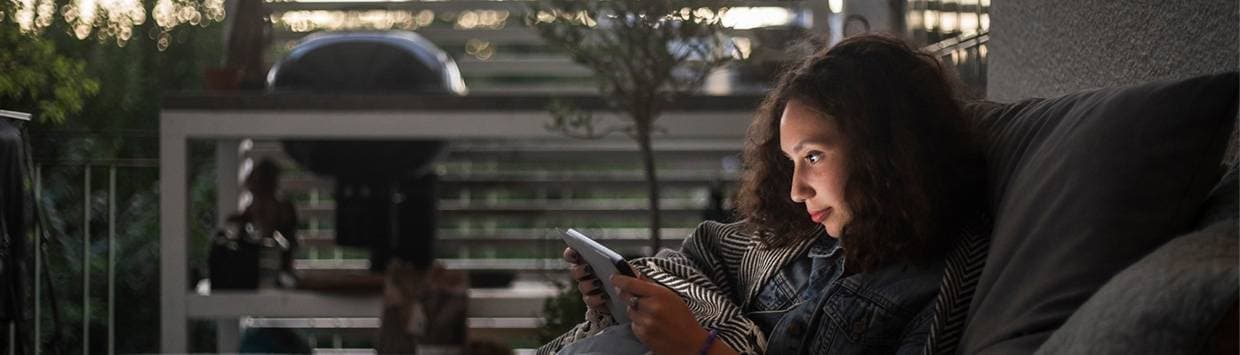 Kvinna som sitter i mörkret i en soffa och kollar på en läsplatta