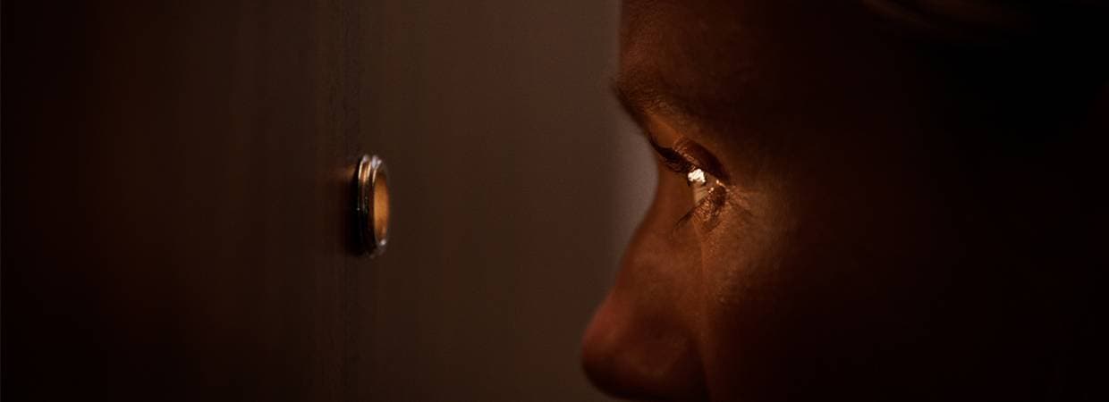 Person som tittar ut genom ett titthål i en dörr