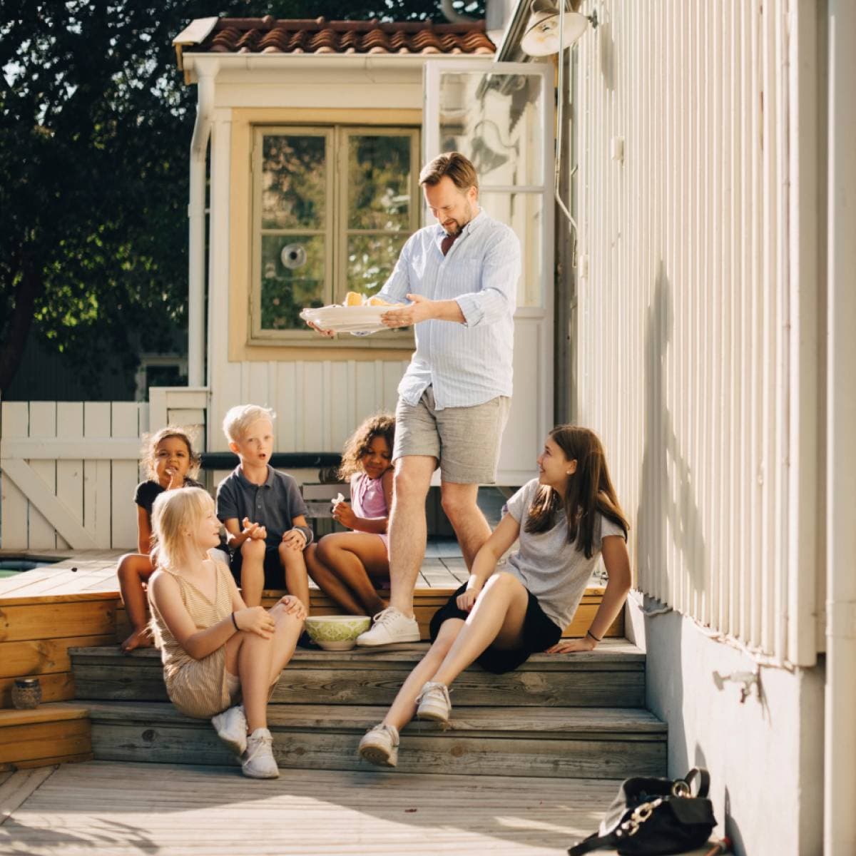 Man med ett fat i händerna går ner för en trappa där några barn sitter.