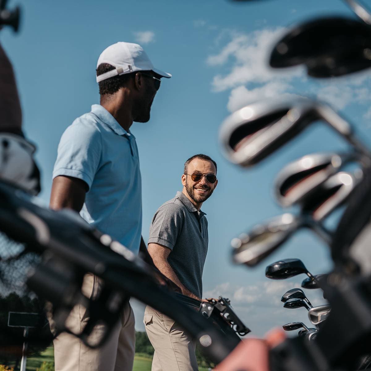 Två killar ler till varandra bakom några golfbagar med klubbor.