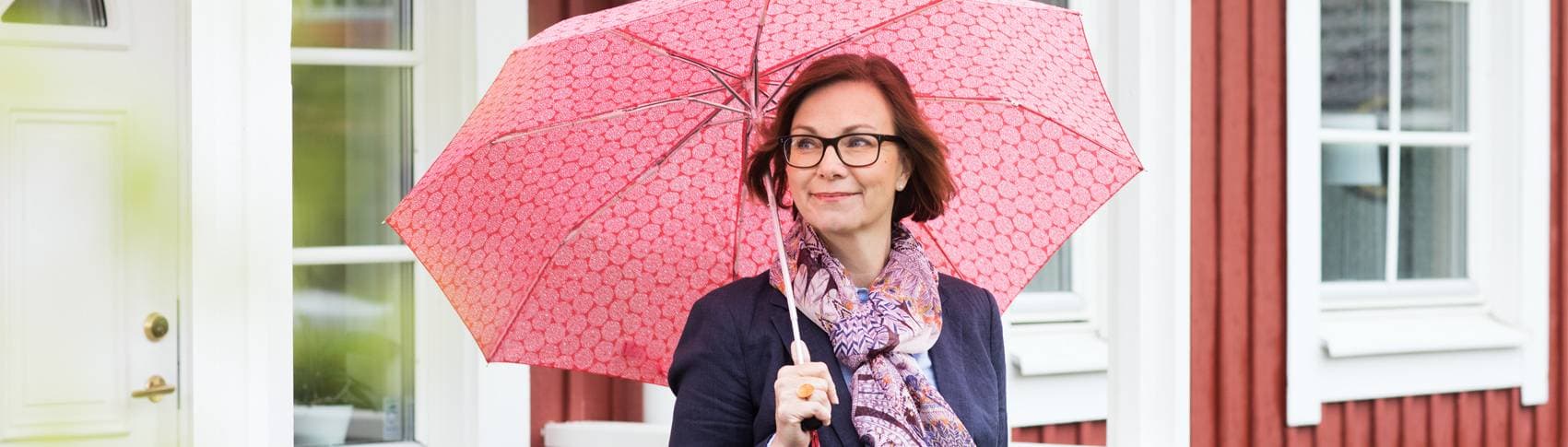 Kvinna i glasögon står under rosa paraply.