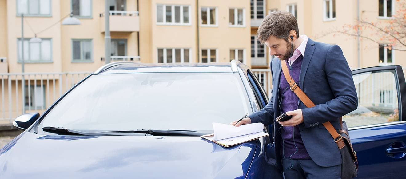 En person vid en bil bläddrar igenom några papper.