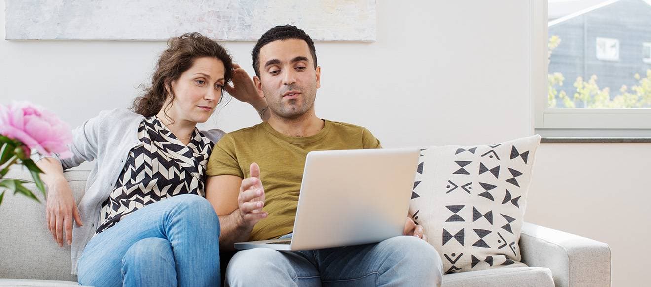 En kvinna och en man sitter i en soffa och mannen har en laptop i sitt knä.
