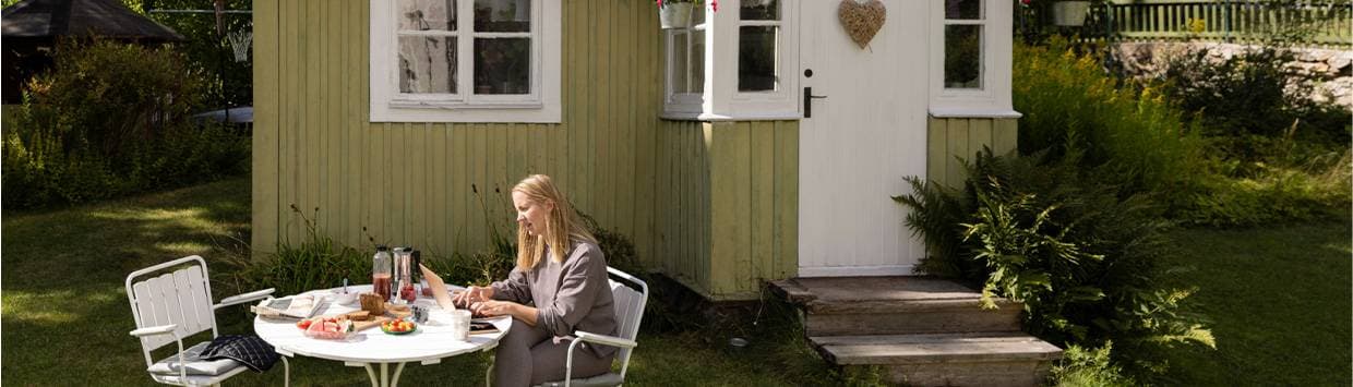En kvinna sitter vid en dator utanför ett grönt sommarhus.