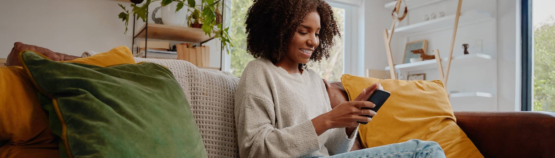 Kvinna sitter i soffa och läser på sin mobil