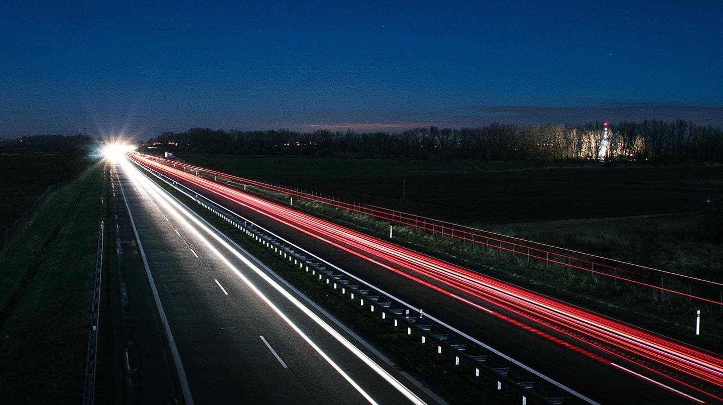 Upplyst bilväg med vägräcken.