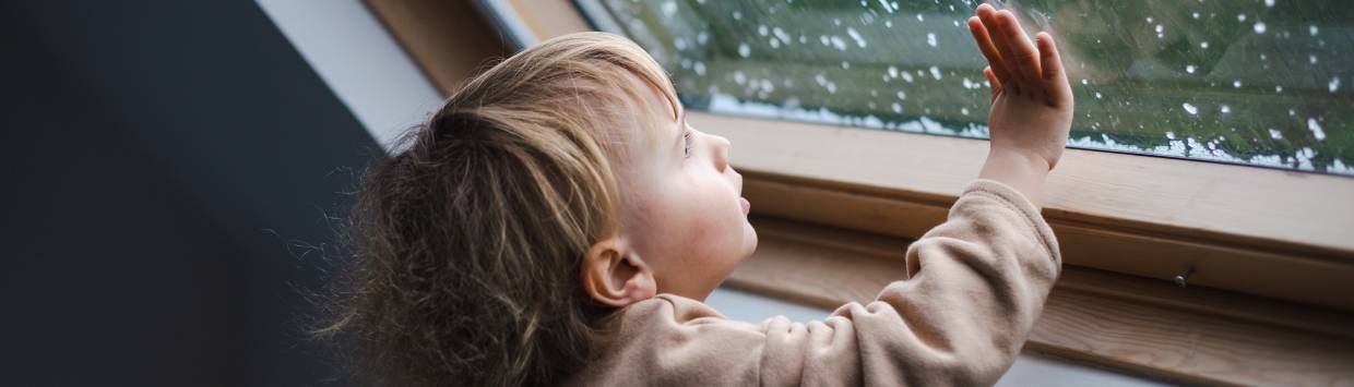 Ett barn tittar ut genom ett fönster samtidigt som det håller handen mot fönstret