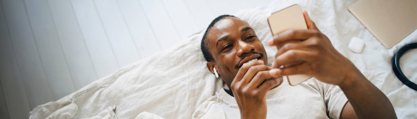 En man ligger i sängen kollar sin mobil.