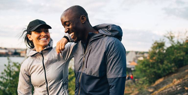 En leende tjej och kille har träningskläder och står nära vatten